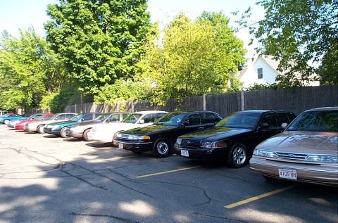 1991 Ford LTD Crown Victoria - Photograph of a row of parked full-size sedans along a wooden fence.