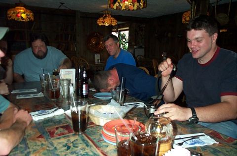 1991 Ford LTD Crown Victoria - A group of friends gather around a table laden with drinks and food in a rustic dining establishment.