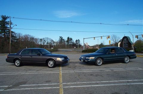 1991 Ford LTD Crown Victoria - Two sedans, likely Mercury Grand Marquis models, are parked next to each other in a parking lot under a blue sky.