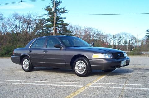 1991 Ford LTD Crown Victoria - This Ford Crown Victoria features a dark gray exterior and is parked in an outdoor lot with trees in the background.