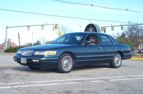 1991 Ford LTD Crown Victoria - This dark green sedan, likely a 1992 model, is parked at an intersection with traffic lights overhead.