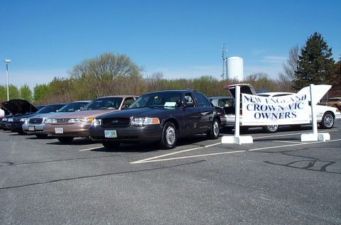 1991 Ford LTD Crown Victoria - A line of Ford Crown Victorias are parked in a lot, with a banner for "New England Crown Vic Owners" visible.