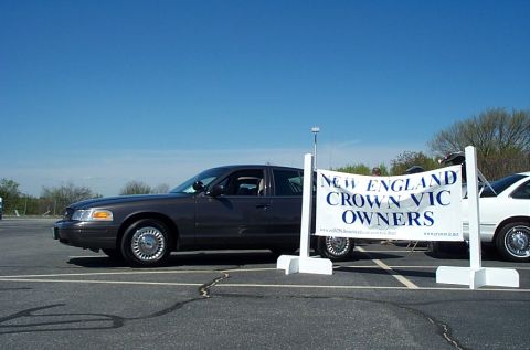 1991 Ford LTD Crown Victoria - A dark gray 1991 Ford Crown Victoria LTD is parked next to a banner for the "New England Crown Vic Owners" club.