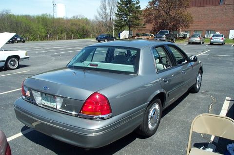 1991 Ford LTD Crown Victoria - A gray Ford Crown Victoria is parked in a lot with other vehicles and trees in the background.