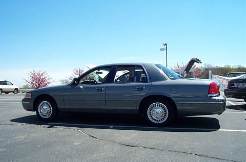 1991 Ford LTD Crown Victoria - A gray Ford Crown Victoria is parked in a lot on a sunny day, with its trunk open.