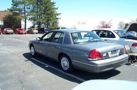 1991 Ford LTD Crown Victoria - A gray sedan is parked in a lot with other vehicles, some with hoods open.