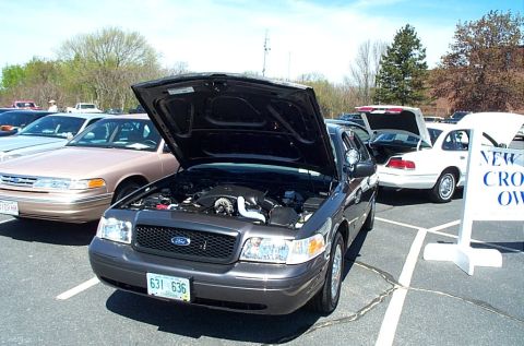 1991 Ford LTD Crown Victoria - Several Ford Crown Victorias parked at an outdoor event, one with its hood open.