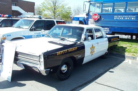 1991 Ford LTD Crown Victoria - A vintage Plymouth Fury police car is parked next to a modern police SUV and a blue bus.