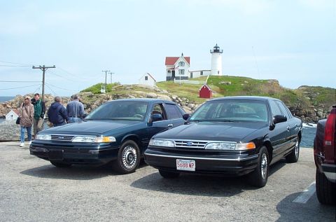 1991 Ford LTD Crown Victoria - Two Ford Crown Victorias are parked near a lighthouse on a sunny day.