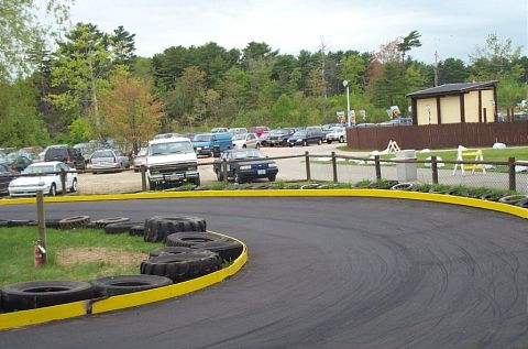 1991 Ford LTD Crown Victoria - A variety of vehicles are parked in a lot adjacent to a race track.