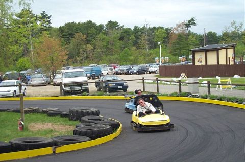 1991 Ford LTD Crown Victoria - Go-karts race around a track with a variety of vehicles parked nearby.