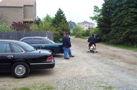 1991 Ford LTD Crown Victoria - Two Ford Crown Victorias are parked on a gravel road while a person rides a scooter.