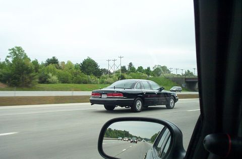1991 Ford LTD Crown Victoria - Rear view of a black 1991 Ford Crown Victoria LTD on the highway, with other vehicles visible in the side mirror.
