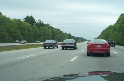 1991 Ford LTD Crown Victoria - Several cars are driving on a highway under an overcast sky.