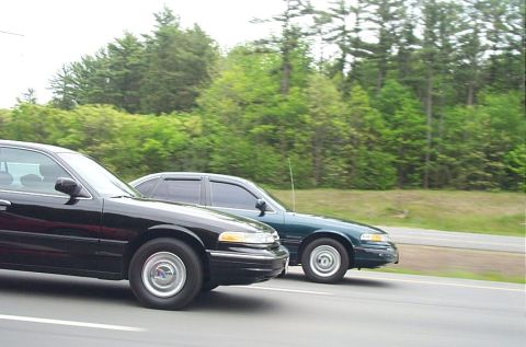 1991 Ford LTD Crown Victoria - Two Ford Crown Victoria sedans are seen from the side, driving on a road with trees in the background.