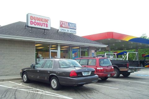 1991 Ford LTD Crown Victoria - A police-style sedan is parked in front of a Dunkin' Donuts, with other vehicles at a gas station behind it.