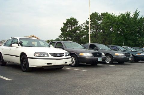 1991 Ford LTD Crown Victoria - Several police sedans are parked in a lot, showing their front ends.
