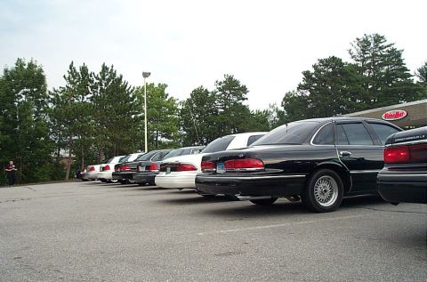 1991 Ford LTD Crown Victoria - Several Ford Crown Victoria sedans are parked in a lot, with trees and a building in the background.