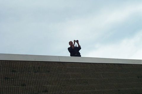 1991 Ford LTD Crown Victoria - A person is on top of a building, holding a phone to take a photo of the sky.