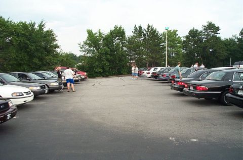 1991 Ford LTD Crown Victoria - A parking lot scene a variety of vehicles, including several black sedans and a red truck, under an overcast sky.