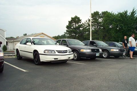 1991 Ford LTD Crown Victoria - A line of police cars, including a Chevrolet Impala and Ford Crown Victorias, parked in a lot.