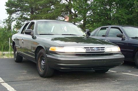 1991 Ford LTD Crown Victoria - A dark green sedan is parked on asphalt, with another vehicle to its right.