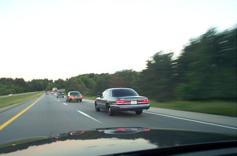 1991 Ford LTD Crown Victoria - A dark 1991 Ford Crown Victoria LTD sedan travels down a highway, seen from behind.