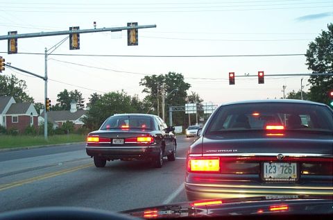 1991 Ford LTD Crown Victoria - Rear view of a dark sedan with distinctive horizontal taillights and chrome accents, driving on a road.