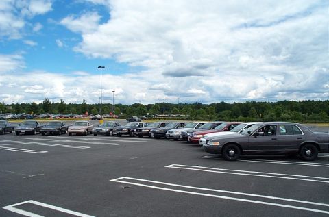 1991 Ford LTD Crown Victoria - A line of sedans, including a dark grey Ford Crown Victoria LTD, parked in a lot under a cloudy sky.