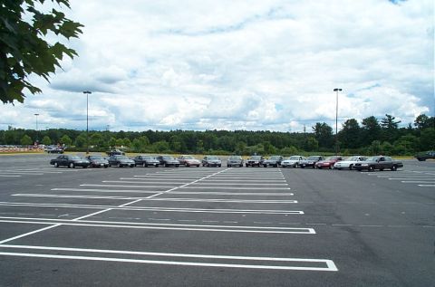 1991 Ford LTD Crown Victoria - A row of sedans are parked in a large, mostly empty parking lot under a cloudy sky.