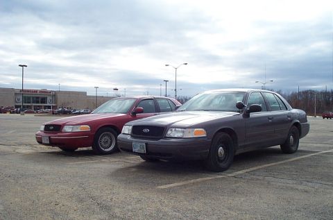 1991 Ford LTD Crown Victoria - Two Ford Crown Victoria police interceptors parked in a lot with a building in the background.