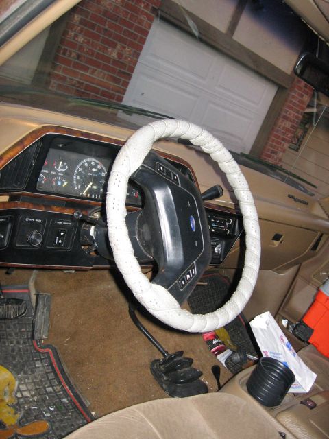 1987 Ford Bronco - The dashboard and steering wheel of a vehicle are visible, with a garage door reflected in the windshield.
