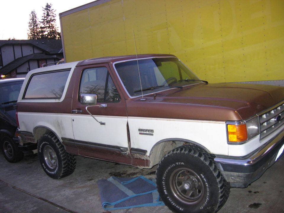 Brown and white 1987 Ford Bronco parked next to a yellow wall