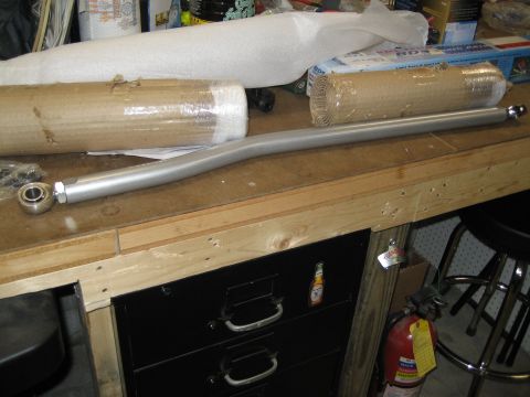 1996 Ford Bronco - A metal steering linkage part rests on a workbench next to wrapped items and a fire extinguisher.