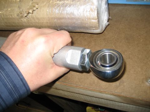 1996 Ford Bronco - A hand grips a silver metal automotive tie rod end, revealing its spherical bearing component.
