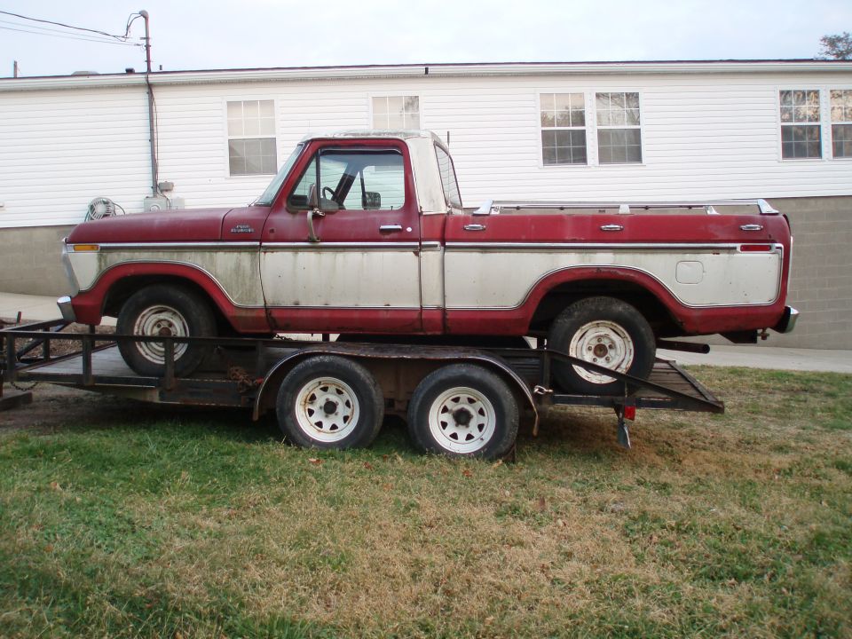 Side view of a red and silver 1977 Ford F-100 pickup truck on a trailer
