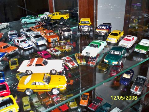 2004 Ford Mustang - A collection of various toy cars displayed on glass shelves, with a prominent yellow 1979 Ford Mustang model in the foreground.