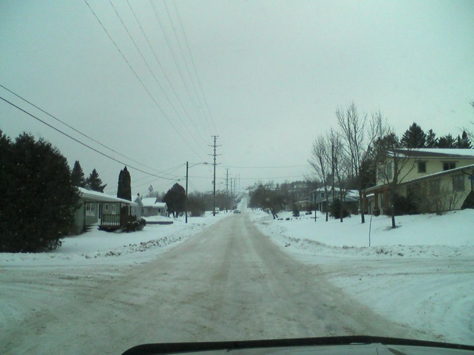 Snowy street with houses and power lines, view from a vehicle