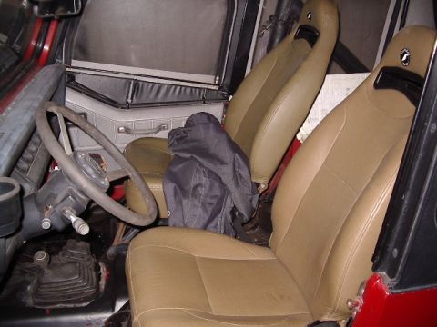 1987 Jeep YJ - The interior of a 1987 Jeep YJ features tan seats, a dark steering wheel, and a manual transmission shifter.