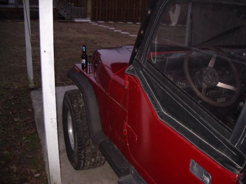 1987 Jeep YJ - A red Jeep CJ is parked next to a white post, with a beer bottle resting on its hood.