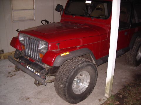 1987 Jeep YJ - A red 1987 Jeep YJ is viewed from the front three-quarter angle, showing its distinctive grille and body style.