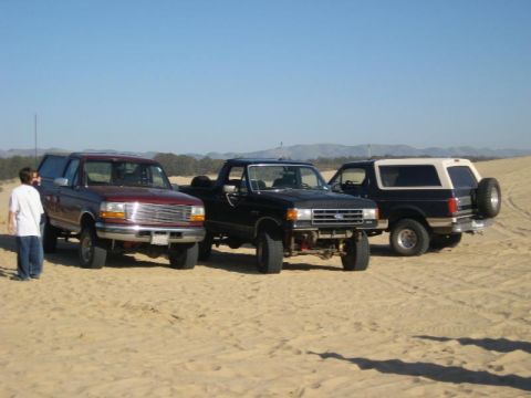 1989 Ford Bronco - Three SUVs are parked on sand dunes with a person standing near the front left vehicle.