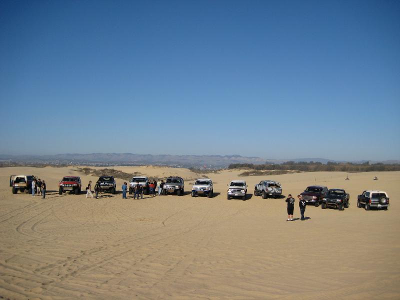 Line of SUVs and trucks on sand dunes under a clear blue sky