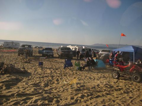 1989 Ford Bronco - A group of vehicles and camping gear are set up on a sandy beach near the ocean.
