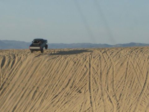 1989 Ford Bronco - Truck driving over a sand dune with tire tracks in the foreground.