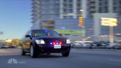 1993 Ford Taurus - A black police car with red and blue lights is captured in motion on a city street.