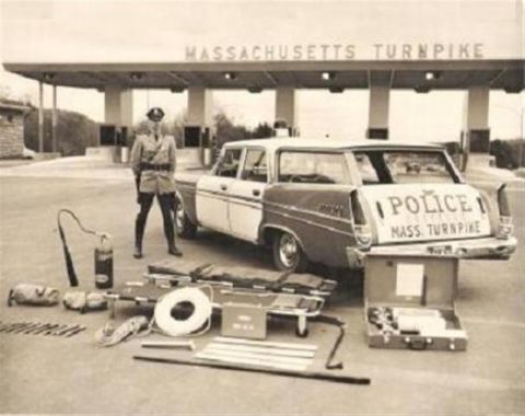 1991 Ford Crown Victoria - A Massachusetts Turnpike police officer stands beside a station wagon, with equipment laid out on the ground.