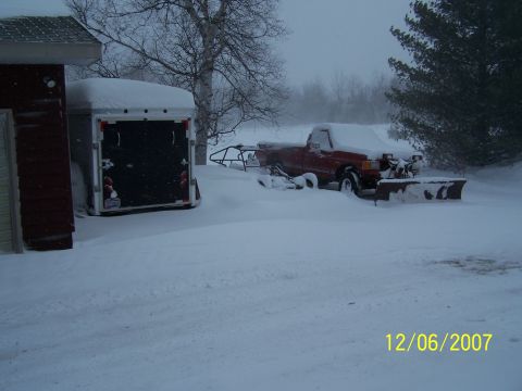 1989 Ford F-150 - Red 1989 Ford F-150 pickup truck equipped with a snow plow sits buried in snow next to a trailer.
