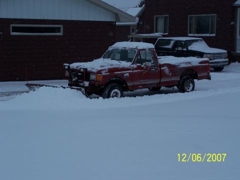 1989 Ford F-150 - A red 1989 Ford F-150 pickup truck is equipped with a snow plow and is clearing a snowy driveway.