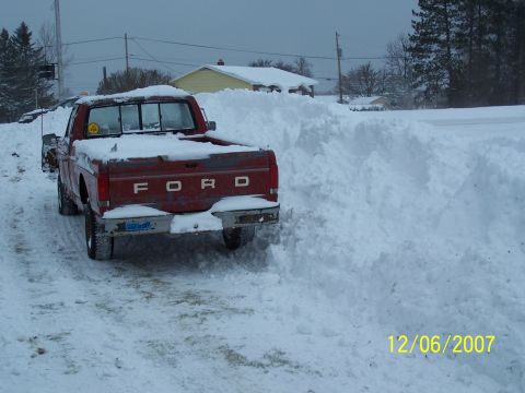 1989 Ford F-150 - A red Ford pickup truck is partially buried in snow, seen from the rear.